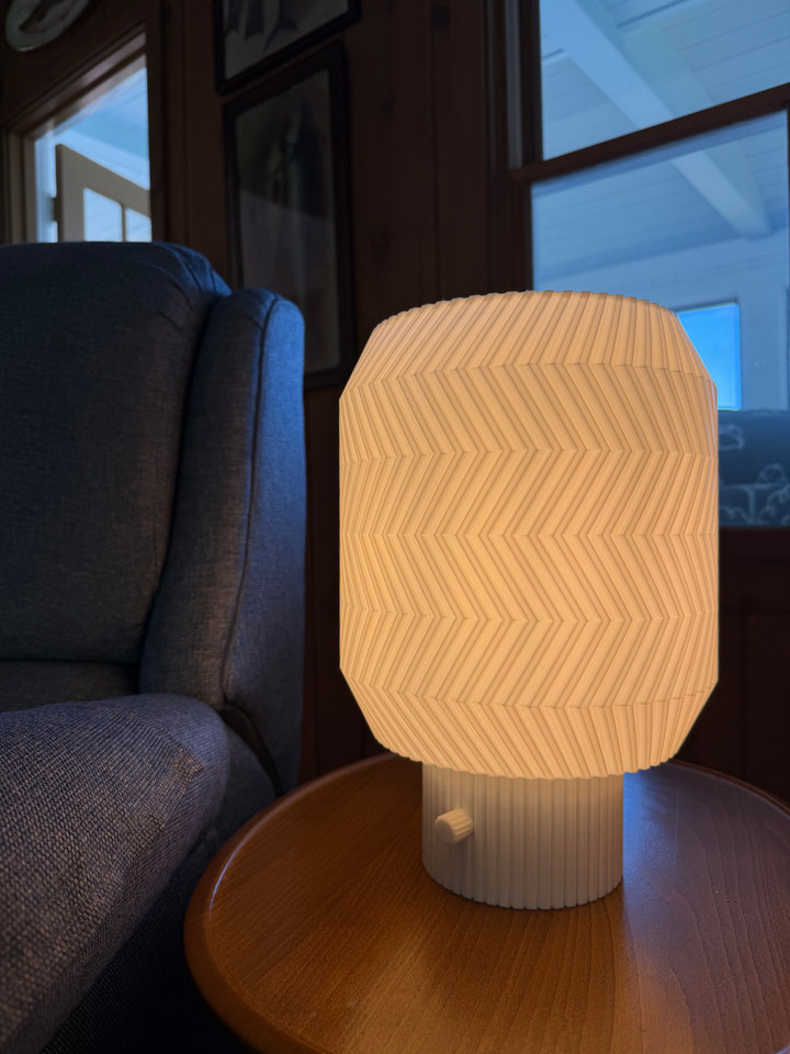 Origami Lamp glowing on a round side table beside an armchair