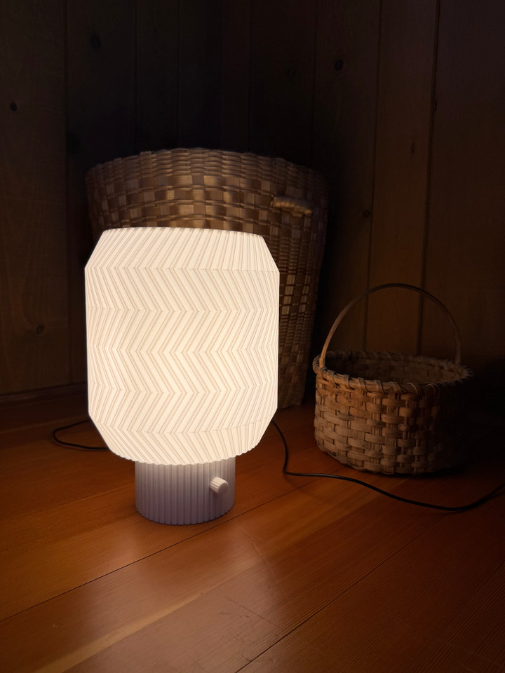 Origami Lamp glowing on a wooden floor beside woven baskets