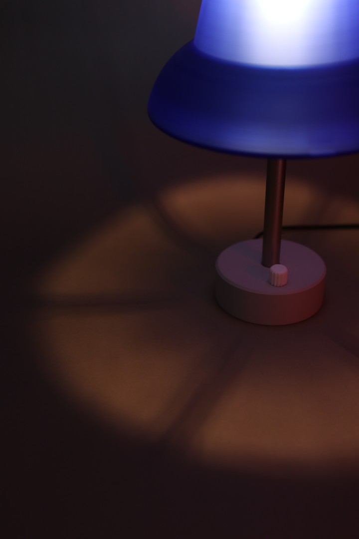 Close view of a blue Pushpin Lamp base and rotary control casting shadows